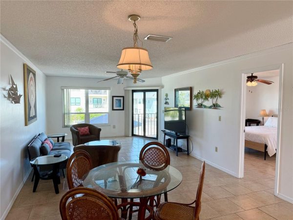Cozy living room and dining area with glass-topped table, wicker chairs, gray sofa, and a wall-mounted TV near a glass door to the balcony.