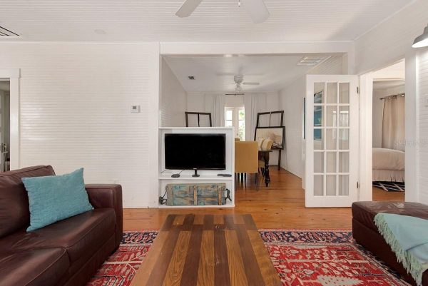 Living room with brown leather sofas, turquoise pillows, and a wooden coffee table on a red patterned rug; TV on a white stand facing seating area.