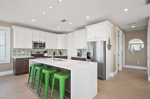 Bright modern kitchen with white upper cabinets, dark lower cabinets, stainless steel appliances, and a white island with four green stools.