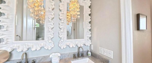 Two large white ornate framed mirrors above a marble double-sink vanity with brushed-nickel faucets.