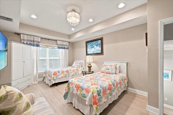 Twin bedroom with two white headboards, sea-themed quilts, a white dresser, and a large window with white curtains.",