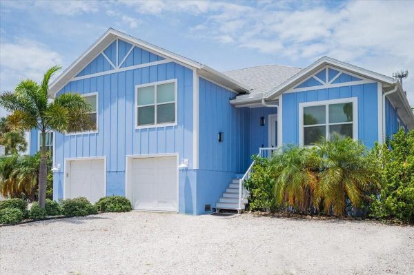 Blue coastal-style house with white trim, two garages, and a front staircase under a sunny sky.