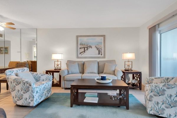 Living room with a beige sofa, two floral armchairs, a dark wood coffee table, and a beach-themed painting above the sofa.