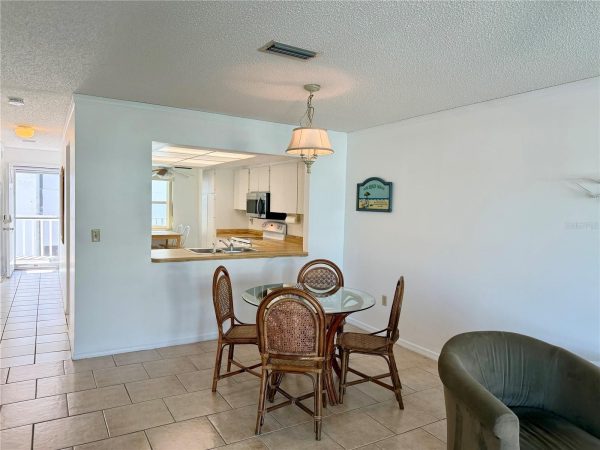 Dining area with glass table and wicker chairs, open pass-through to a white kitchen.