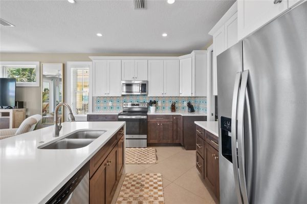 Bright modern kitchen with white cabinets, stainless appliances, and a patterned aqua tile backsplash reading across the counters.