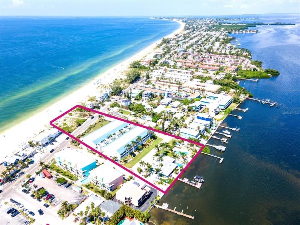 Aerial view of a beachfront property outlined in magenta, showing a road, palm trees, and white sand next to the ocean.