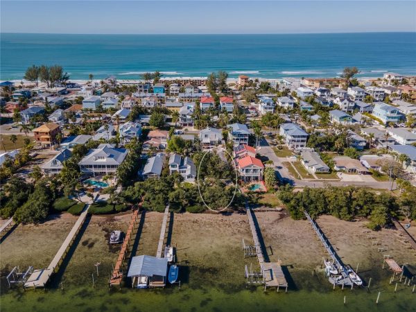 Aerial view of a coastal residential neighborhood with houses, palm trees, and a sandy beach along the ocean fronting a blue sea.