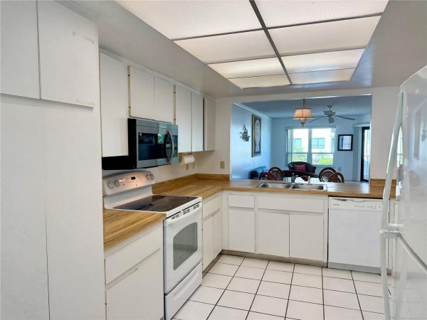 Bright white kitchen with wood countertops, white cabinets, electric range and microwave, and a pass-through to the living/dining area.