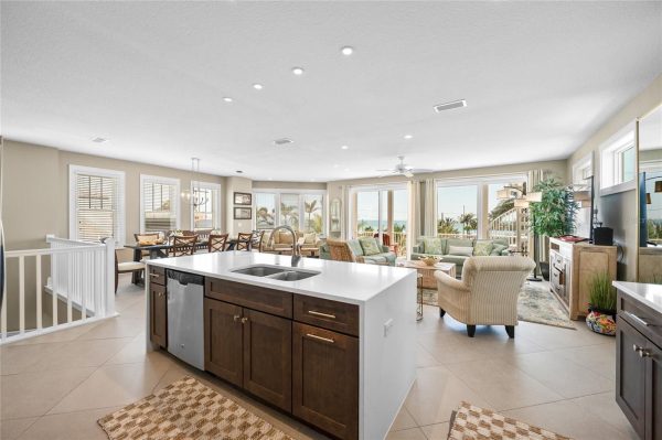Open-concept living area with a large kitchen island, dining table, and lounge seating, overlooking a sunny coastal view.