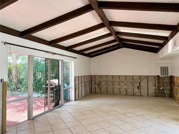 Open living area under renovation with dark wood ceiling beams, large sliding glass doors to an outdoor patio, and exposed wall framing along the lower walls.