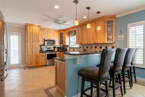 Bright kitchen with light wood cabinets, stainless steel appliances, and a blue island with four cushioned bar stools.