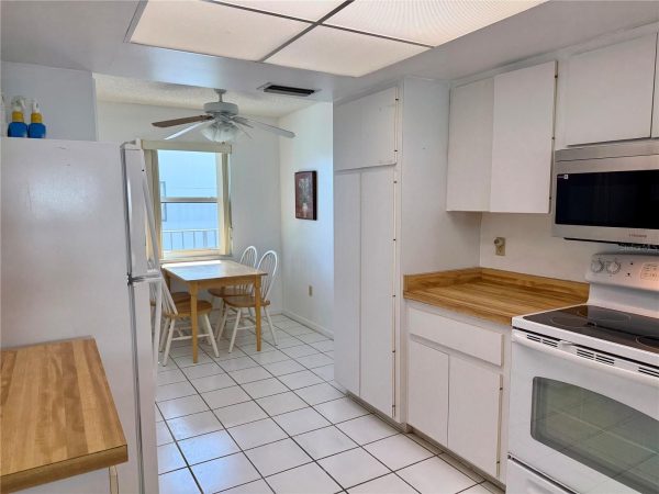 Bright white kitchen with tiled floor, white cabinets, wooden countertops, and a small dining nook by a window with a wooden table and white chairs.