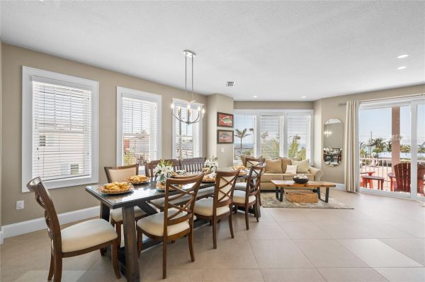 Bright open-concept dining room and living area with a dark wood table set for a meal, chandelier overhead, and a seaside balcony view from large windows.