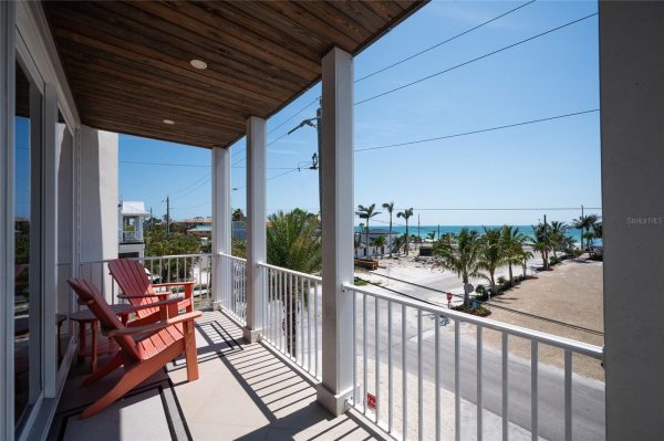 Balcony with two red Adirondack chairs overlooking a palm-lined street toward the ocean.
