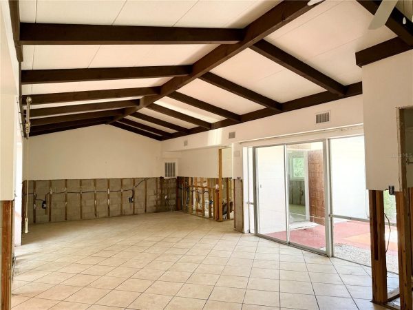 Open-concept room under renovation with dark exposed wooden beams and large sliding glass doors to the outside patio.