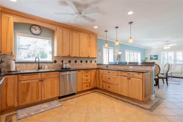 Open-concept kitchen with light wood cabinets, granite counters, and a blue accent wall flowing into a living area.