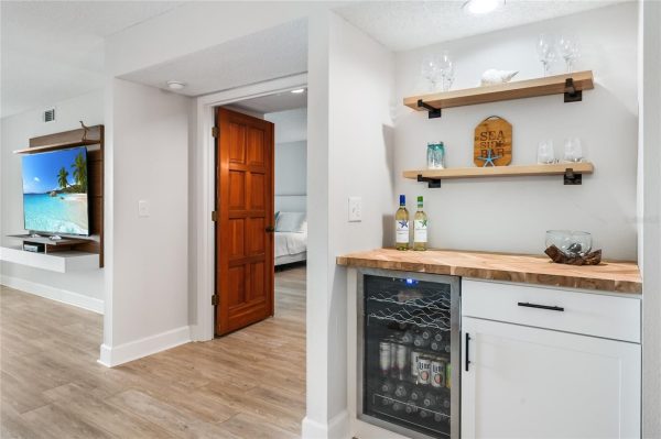 Living area with a wall-mounted TV on a wooden entertainment unit beside a doorway to a bedroom.