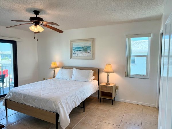 Cozy coastal bedroom with a queen bed, two nightstands, matching lamps, and a beach scene artwork above the headboard