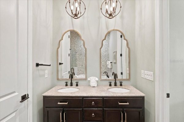 Double bathroom vanity with two undermount sinks, dark wood cabinet, speckled countertop, and arched framed mirrors.