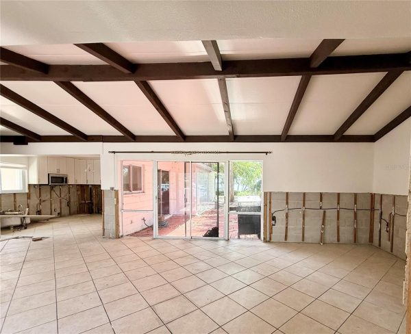 Open living area under exposed dark wooden ceiling beams, with a tiled floor and partially finished walls showing exposed studs.