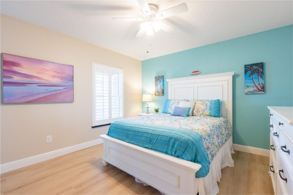 Bright coastal bedroom with a white wooden bed, teal accent wall, and colorful patterned bedding; ocean-themed artwork on walls and a white dresser nearby.