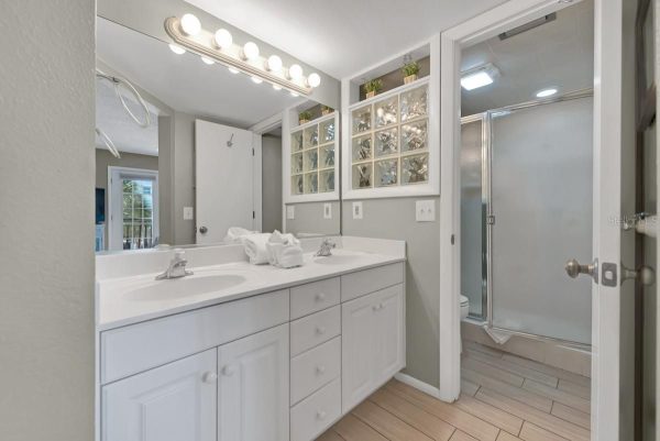 Bright white double-sink vanity with a large mirror, towel stack, and a glass-block window; glass-door shower to the right.