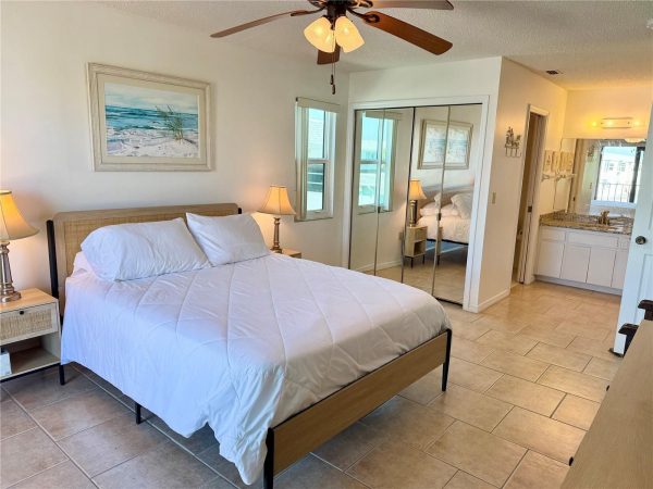Bedroom with a queen bed, white quilt, two nightstands with lamps, and a beach scene painting above the headboard