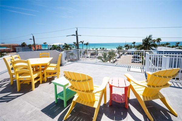 Rooftop patio with bright yellow chairs around a small table, overlooking a beach and palm trees.